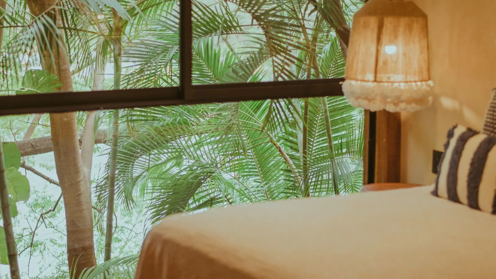 A hotel bed beside a window onto palm trees